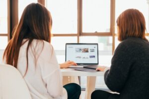 Deux personnes travaillent ensemble sur un ordinateur portable. - Agence web Prism